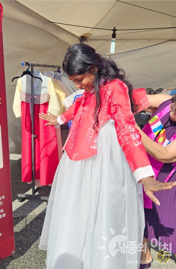 한글 문양이 새겨진 한복을 입어보며 환하게 웃는 외국인 관람객의 모습.세종한글축제 ‘충녕이네 한복가게’에서 한글과 한복의 아름다움을 직접 체험하는 즐거운 순간이다.[사진=이유진기자]